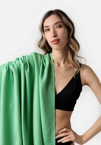 Plaid verde con un design a diamante, caratterizzato da una texture morbida, appoggiato su una spalla, abbinato a un top nero.