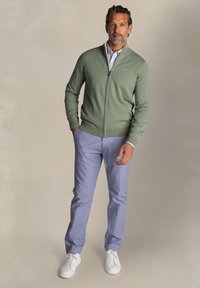 Groene rits sweater, lichtblauw overhemd met patroon, lichtblauwe broek en witte sneakers. Glad textuur met een casual pasvorm.