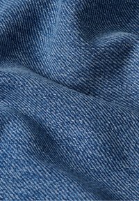 Denimtyg i en medelblå nyans, med en texturerad yta och diagonalt vävda mönster, som visar subtila variationer i ton.