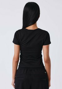 Zwarte aangesloten t-shirt met korte mouwen en een ronde halslijn, gemaakt van een gladde stof, gedragen met losse zwarte broek met zakdetails.