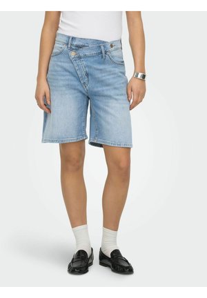 Person som har på seg lys blå denim bermudashorts med overlappende midjebånd, hvite sokker, svarte loafers, hvit skjorte og sølvklokke.