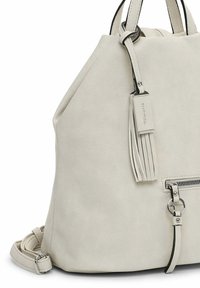 Vaaleabeige nahkainen reppu, jossa on etutasku vetoketjulla, koristeelliset hapsut ja säädettävät olkahihnat.