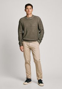 Oliven grøn ribstrikket sweater med rund hals, parret med beige slim-fit bukser og mørke sneakers. En simpel, moderne, afslappet påklædning.