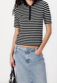 Pánský polo top s krátkým rukávem pruhovaný v černobílé barvě, se zapínacími límcem. Nosit s světle modrou džínsovou sukní. Texturovaná ribová tkanina.