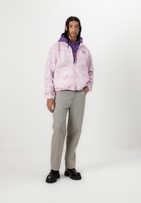 Pink bomber jacket with a wavy pattern, gray sweatshirt underneath, light gray jeans, and black chunky-soled shoes.