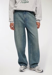 Jeans a gamba larga in denim blu chiaro con un finish sbiadito, vita alta e tasche, abbinati a un hoodie grigio e sneaker argentate.
