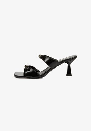 Mules de charol negro con punta cuadrada, que cuentan con tiras entrelazadas y un tacón delgado y angulado. Los detalles incluyen herrajes en color dorado.