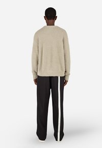 Fényes szürke, bolyhos pulóver kerek nyakkal és hosszú ujjakkal, fekete nadrággal kombinálva, amelyen fehér oldalsáv található.