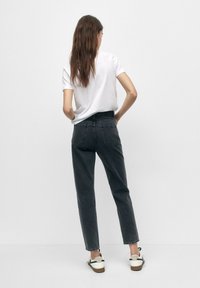 Jeans de tiro alto y pierna recta en denim gris oscuro, con bolsillos traseros y un acabado limpio. Combinados con una camiseta blanca lisa y zapatillas.