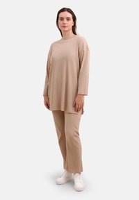 Beige ribbet loungewear sæt bestående af en langærmet top med rund hals og afslappet pasform, sammen med brede bukser. Hvide sneakers.