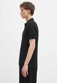 Polo shirt nero con maniche corte, colletto classico e logo discreto. Realizzato in cotone, con una texture liscia, taglio dritto e spacchi laterali.