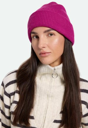 Gorro de canalé rosa brillante con un ajuste ceñido. Llevado con un suéter crema con rayas y cremallera, que presenta un detalle de tirador en forma circular.
