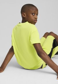 Tricou galben neon cu mânecă scurtă și guler rotund, asortat cu pantaloni scurți. Textură netedă, fără modele sau accente vizibile.
