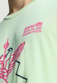 Camiseta atlética de color verde claro con diseños en rosa y azul marino, que incluye el logo del "Maratón de Berlín de BMW" y patrones abstractos. Tejido texturizado.