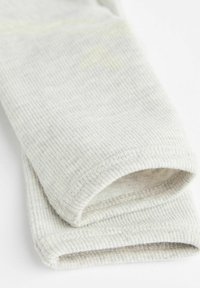 Hellgraue gerippte Socken mit weicher Textur, die einen umgeschlagenen Bund und subtile gelbe Akzente aufweisen. Das Material wirkt gestrickt und nahtlos.