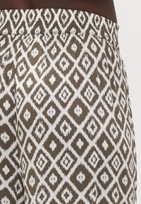 Tissu léger et à motif présentant un design en diamants dans des nuances de brun et de blanc. Taille élastique avec surface texturée.