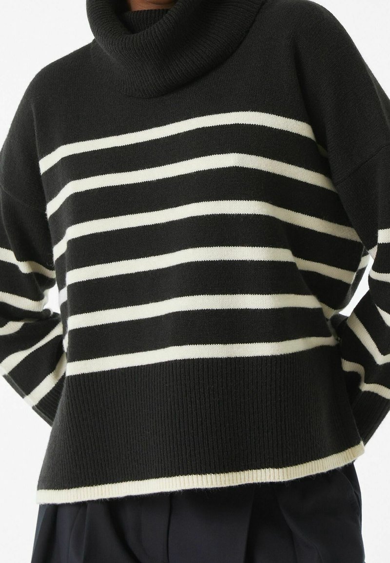 Pull rayé noir et blanc avec un haut col roulé, fabriqué en tissu tricoté doux, présentant une coupe ample et des bords côtelés.