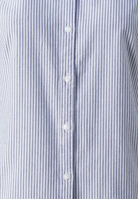 Camicia a righe blu e bianche realizzata in tessuto di cotone, con una chiusura anteriore a bottoni bianchi e una texture liscia.