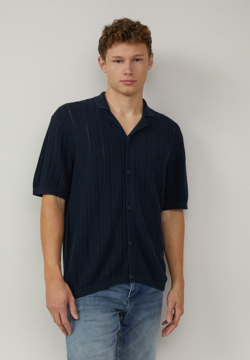 Navyblauwe gebreide shirt met korte mouwen, met een kraag, verticale ribbeltextuur en vijf knoopsluitingen aan de voorkant.