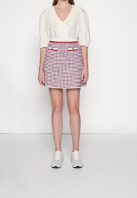 En vit blus med en stickad krage, kombinerad med en röd och vit hundtandsmönstrad kjol med sidofickor. Skorna består av pastellfärgade sneakers.