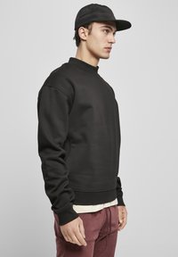 Svart crewneck genser med lange ermer, ribbede mansjetter og en teksturert overflate, parret med burgunder joggebukser og en svart caps.