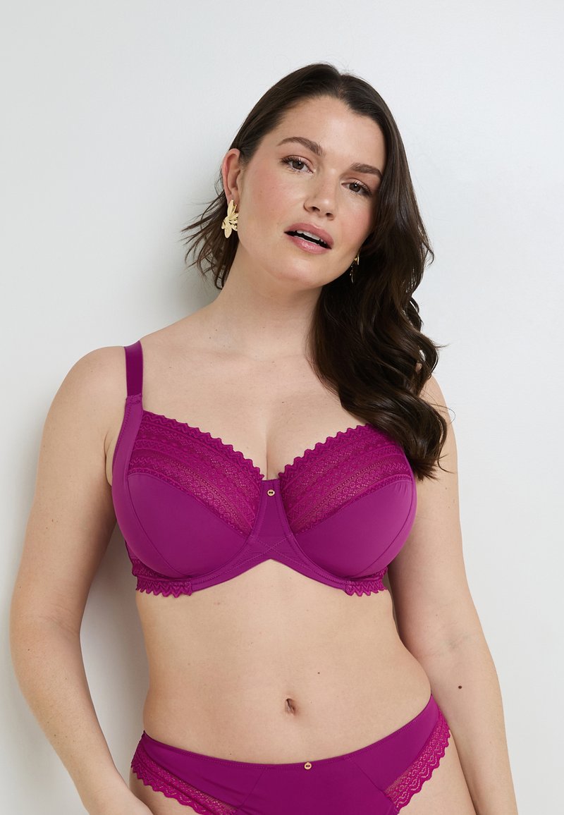 Soutien-gorge viola con bordi in pizzo e una decorazione dorata al centro. Spalline regolabili e un design strutturato per il supporto. Texture liscia.