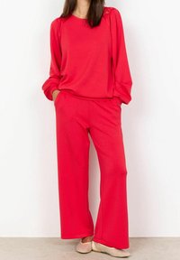 Blusa roja de manga larga con detalles texturizados en los hombros, combinada con pantalones de pierna ancha. Tejido suave con un corte holgado, ideal para un uso cómodo.