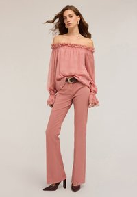 Blusa rosa off-the-shoulder con volant, abbinata a pantaloni a zampa d'elefante su misura e scarpe con tacco. Tessuto dalla trama liscia.