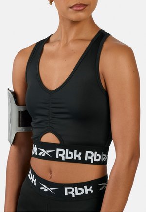 Frau trägt schwarze Reebok-Sportbekleidung mit ärmellosem Oberteil und Leggings und ein graues Armband am linken Arm.