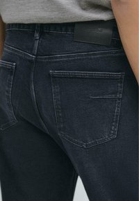 Jeans in denim scuro con una trama liscia, caratterizzati da un leggero sbiadimento, due tasche posteriori e un'etichetta in pelle nera del marchio in vita.
