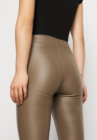 Sydda bruna leggings tillverkade av ett glänsande material, med hög midja och en synlig söm som går ner längs baksidan. Texturerad tyg.