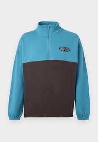 Blå og brun genser med kvart-glidelås krage, elastiske mansjetter, og Rip Curl-logo på brystet. Laget av myk bomullsblanding.