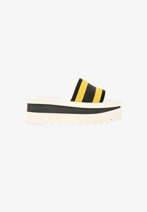 Sandale à plateforme avec semelle blanche épaisse et bride en tissu rayé noire et jaune sur le pied.