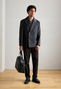 Dubbelzijdige donkergrijze wollen jas, gestructureerde bruine corduroy broek, zwarte leren schoenen en een zwarte leren tas. Soepele, op maat gemaakte ontwerp.