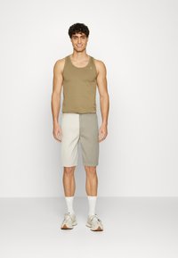 Oliven tanktopp med rund hals, paret med shorts i fargeblokk i lysegrått og mørkegrått. Kule, atletiske joggesko og hvite sokker.