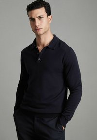 Polo cu mâneci lungi, de culoare bleumarin, cu o textură moale, având un guler clasic, închidere cu trei butoane și manșete ribbate. Design slim fit.