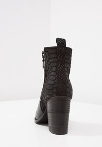 Botines negro con un patrón texturizado de piel de serpiente en la parte trasera, una punta lisa, detalle de cremallera y un tacón robusto y curvado.