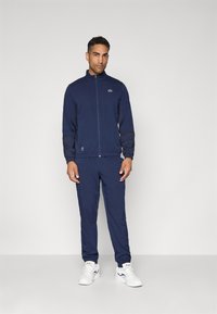 Trening de marin din material ușor, cu jachetă cu fermoar, pantaloni cu talie elastică și detalii subtile cu logo. Asortează-l cu pantofi sport albi.