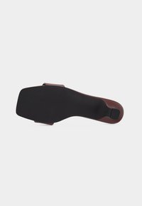 Chaussure en cuir marron à enfiler montrée du dessous avec un bout carré et un talon bas noir sur fond blanc.