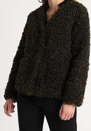 Femme portant une veste polaire marron foncé texturée à manches longues et col montant, associée à un pantalon noir.