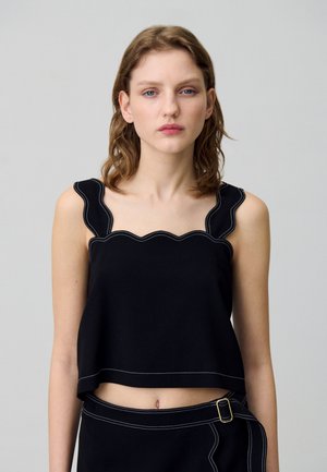 Top noir court avec des bords festonnés et des coutures blanches contrastantes, fabriqué à partir d'un tissu lisse. Associé à une jupe taille haute assortie.