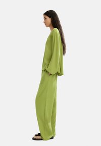 Zielony dwuczęściowy strój składający się z luźnej góry z długim rękawem oraz spodni z szerokimi nogawkami. Wykonany z lekkiego materiału; casualowy styl.