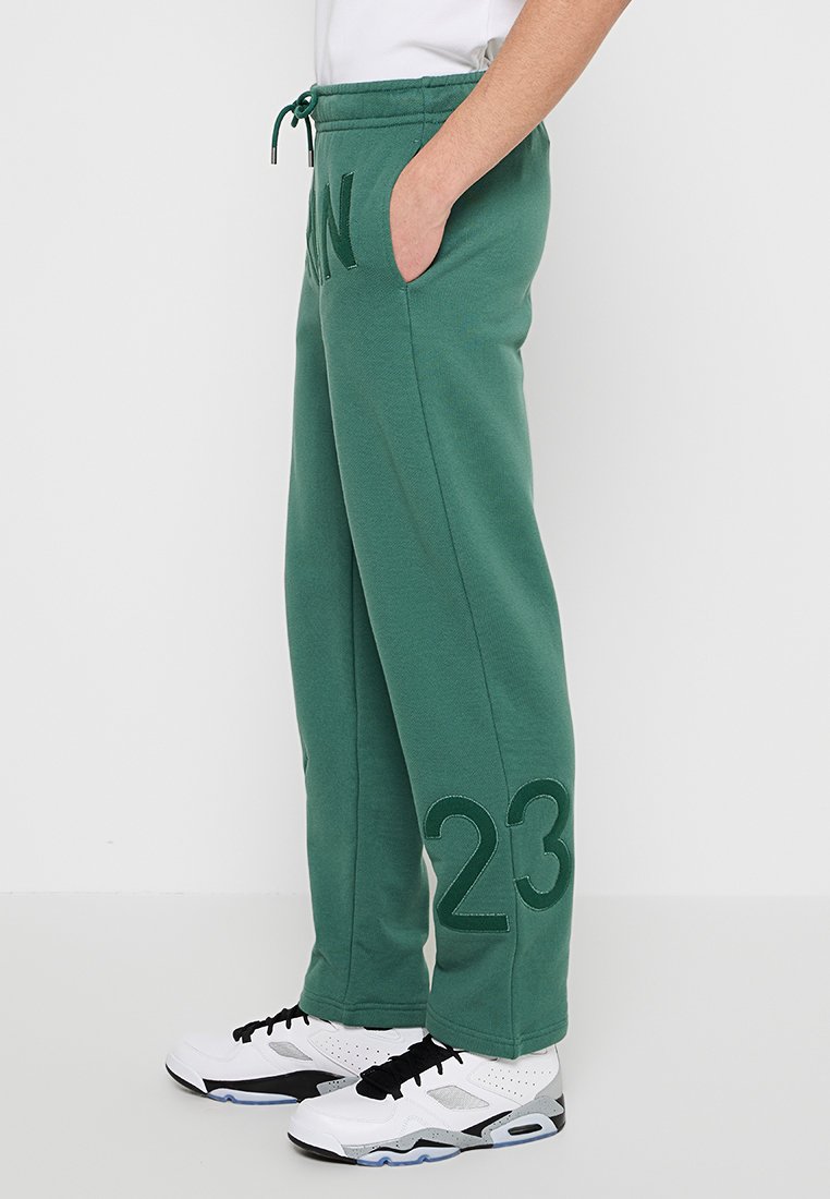 Pantalon de survêtement vert avec une texture côtelée, présentant une taille avec cordon de serrage, des poches latérales et des chiffres brodés "23" ainsi que les initiales "AN."
