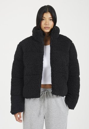 Veste matelassée en fausse fourrure noire avec un col haut, fermeture éclair et une coupe boxy. Présente une surface texturée et des manches larges.