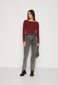 Langermet marnjeblå topp kombinert med høyt liv, falmet grå jeans, svart belte og svarte ankelboots. Modellen holder en liten svart håndveske.