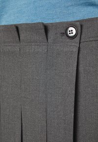 Pantalon gris plissé avec un bouton noir sur la ceinture, porté avec un haut bleu clair.