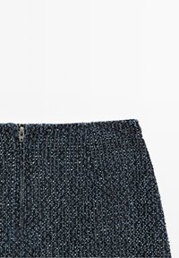 Tissu texturé bleu foncé avec des taches argentées et bleu clair, présentant une fermeture éclair argentée fermée au centre de la section supérieure.