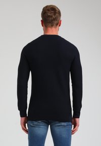 Granatowy sweter z dzianiny z długimi rękawami, z ribbowanym dołem i teksturowanym materiałem, przedstawiony z tyłu w połączeniu z jasnoniebieskimi dżinsami.