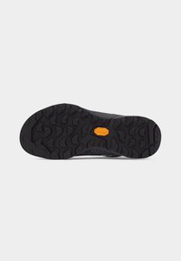 Semelle noire robuste avec des crampons profonds et un logo orange Vibram au centre, conçue pour une meilleure adhérence et traction.