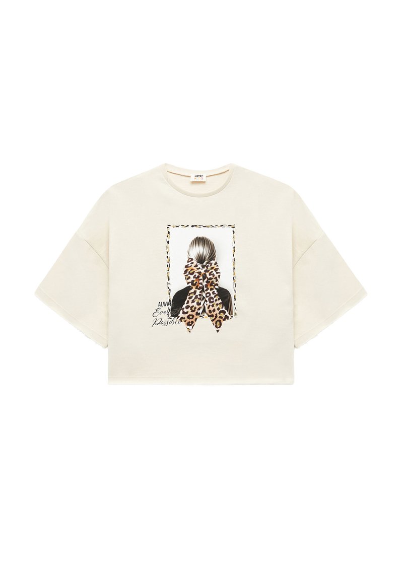Afkortet creme t-shirt med korte ærmer, der har et grafisk motiv af en figur med en leopardmønstret sløjfe og tekst under billedet.